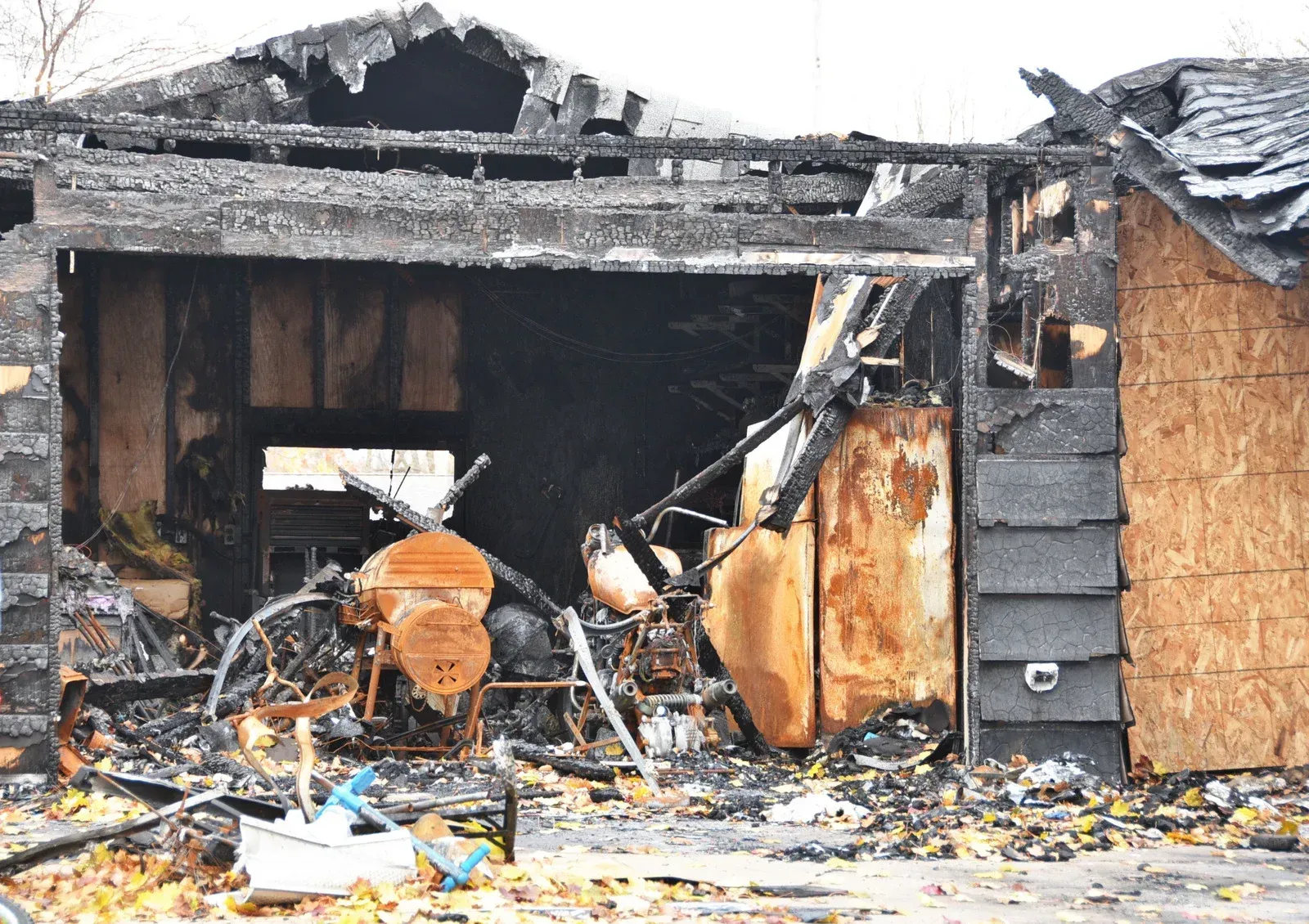 A burned garage with charred wood, debris, and exposed interior. Shingles and plywood are visible.
