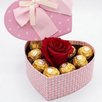 Pequeña caja de regalo con flores rosas y blancas, un osito de peluche y bombones envueltos sobre una mesa.