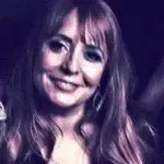A woman with long hair is smiling in a dark room.