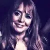 A woman with long hair is smiling in a dark room.
