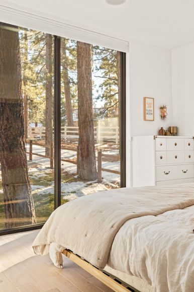 A bedroom with a bed and a large window with a view of trees.