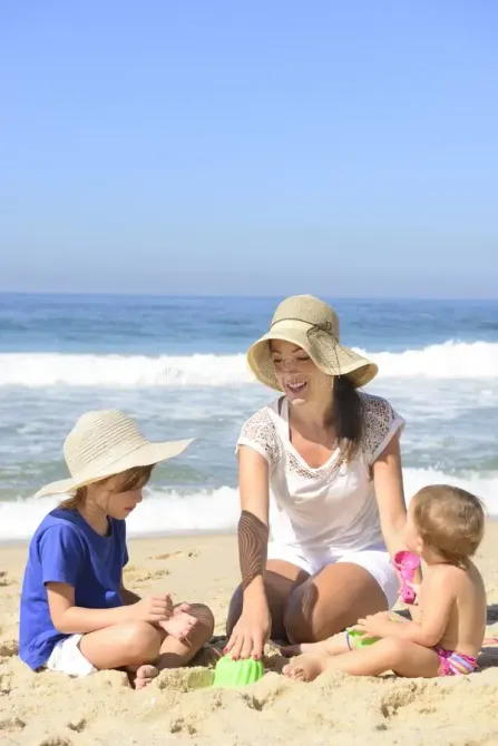 a woman and two children are sitting on the beach playing in the sand.