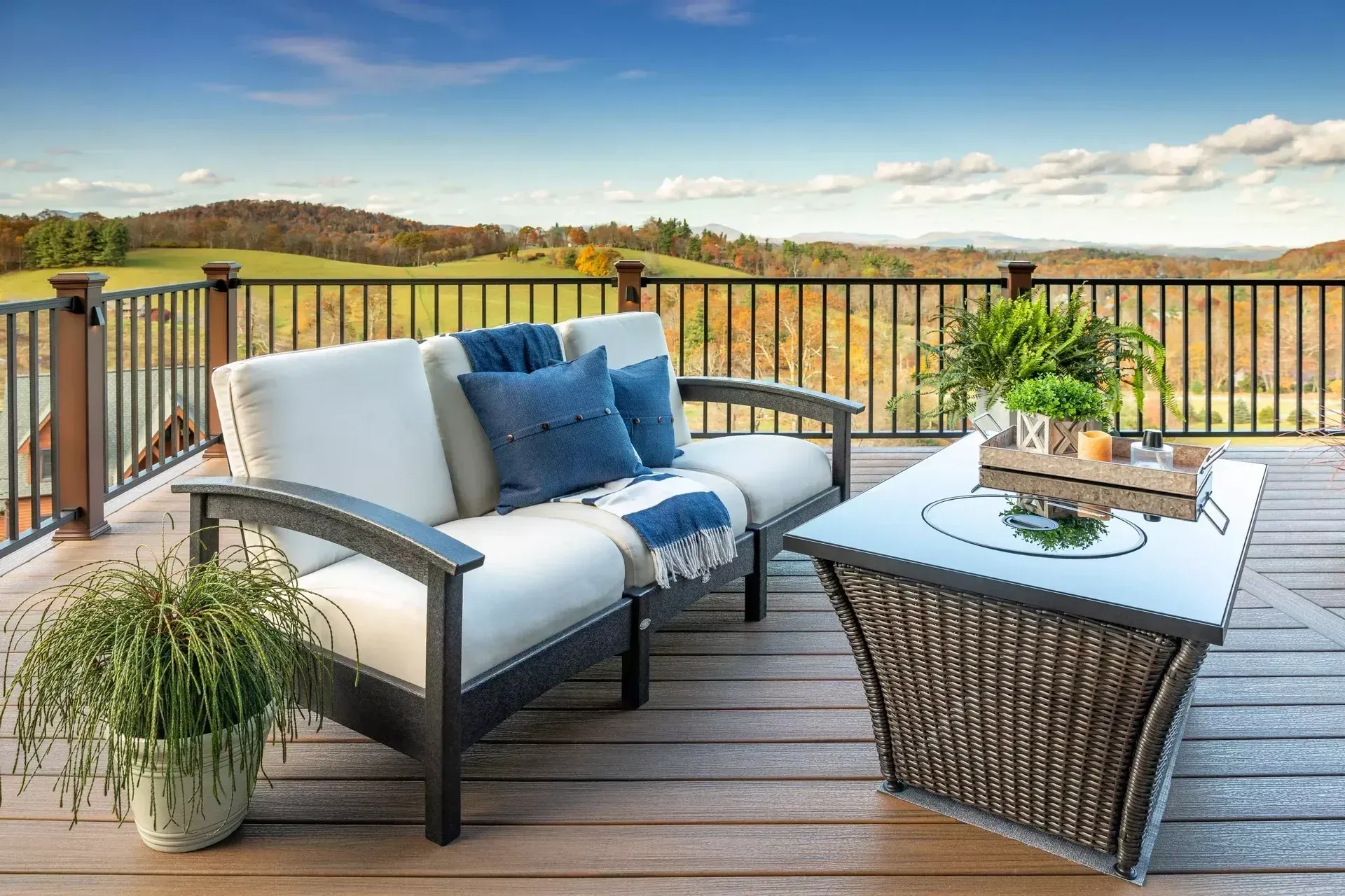 A modern outdoor sofa with cream cushions and blue pillows, paired with a rattan coffee table on a wooden deck.