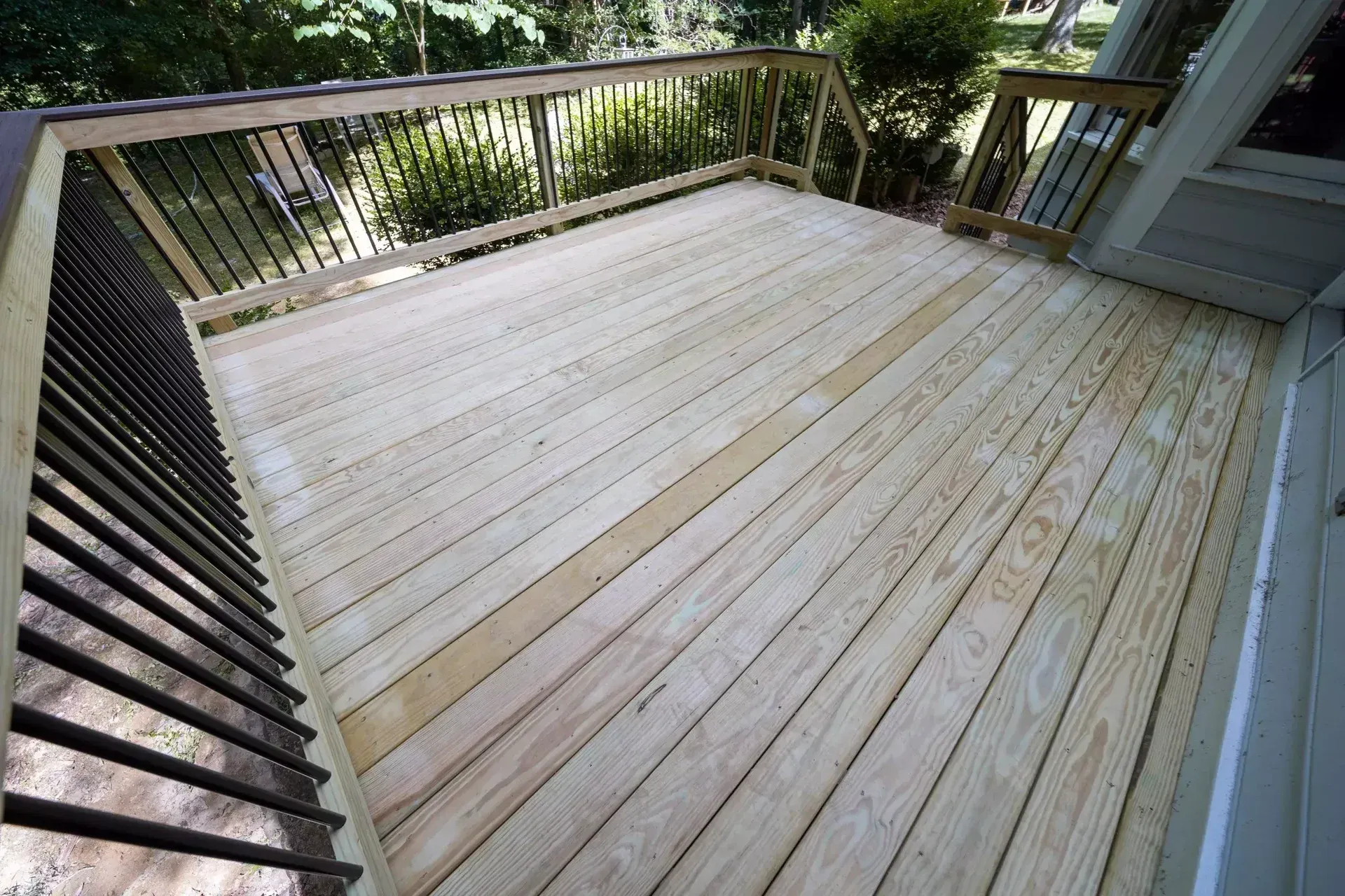 A freshly built wooden deck with light-colored planks and black metal railings, viewed from a slightly elevated angle.
