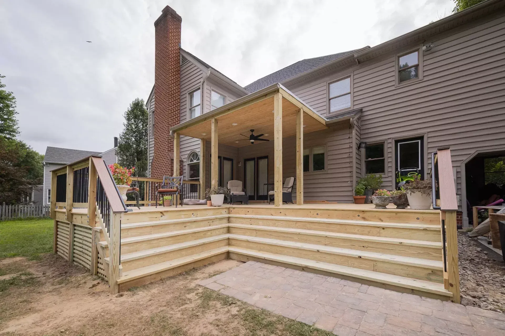 Newly built wooden deck with a covered patio area attached to the back of a light-brown vinyl-sided suburban house.
