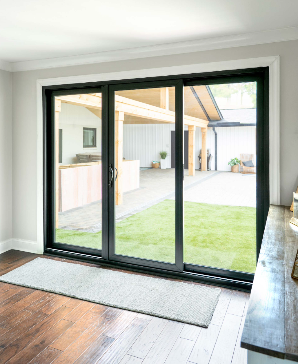 A view through a doorway into a bright living room featuring a grey armchair, a sliding glass door, and a wooden deck.