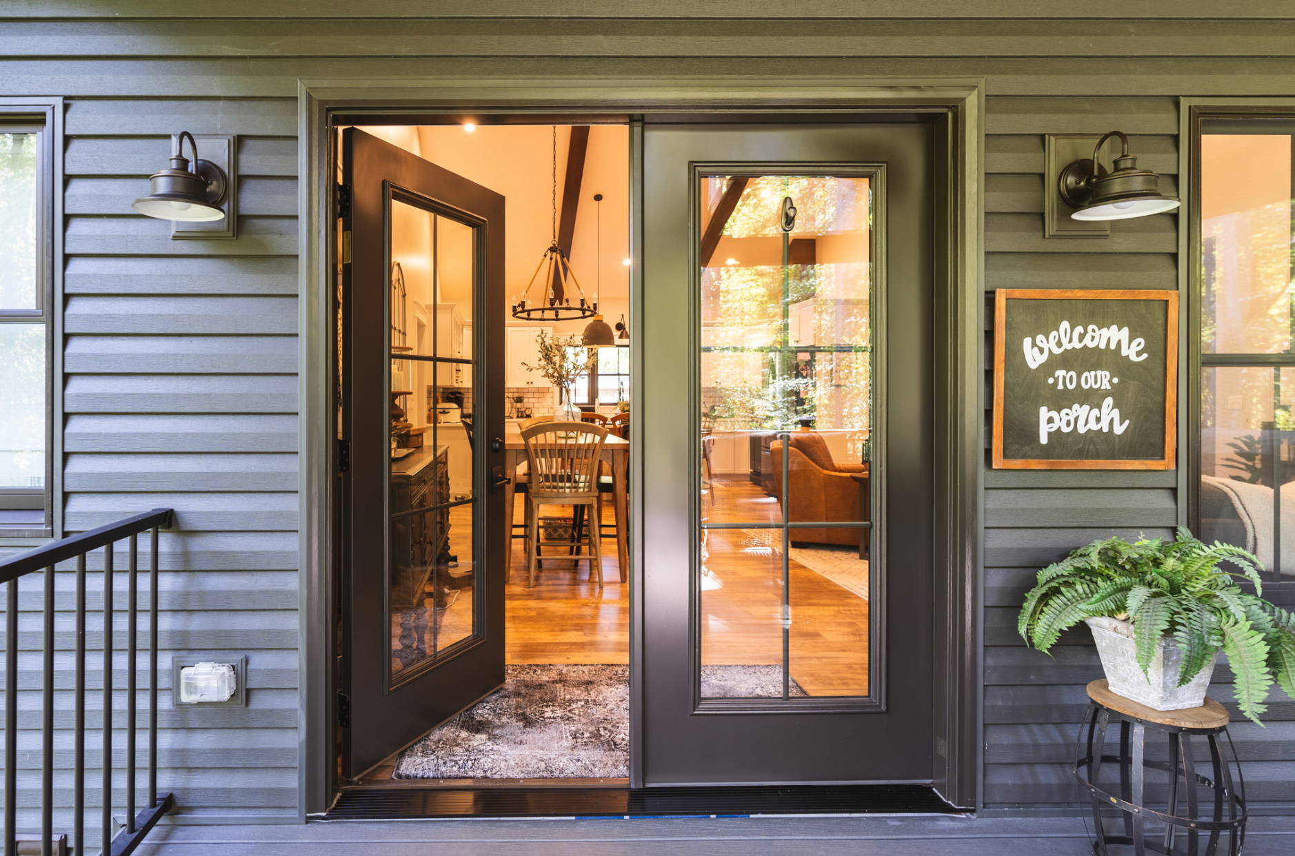 A patio with grey stone tiles and stairs leading to double glass doors on a brick house, bordered by a wooden fence.