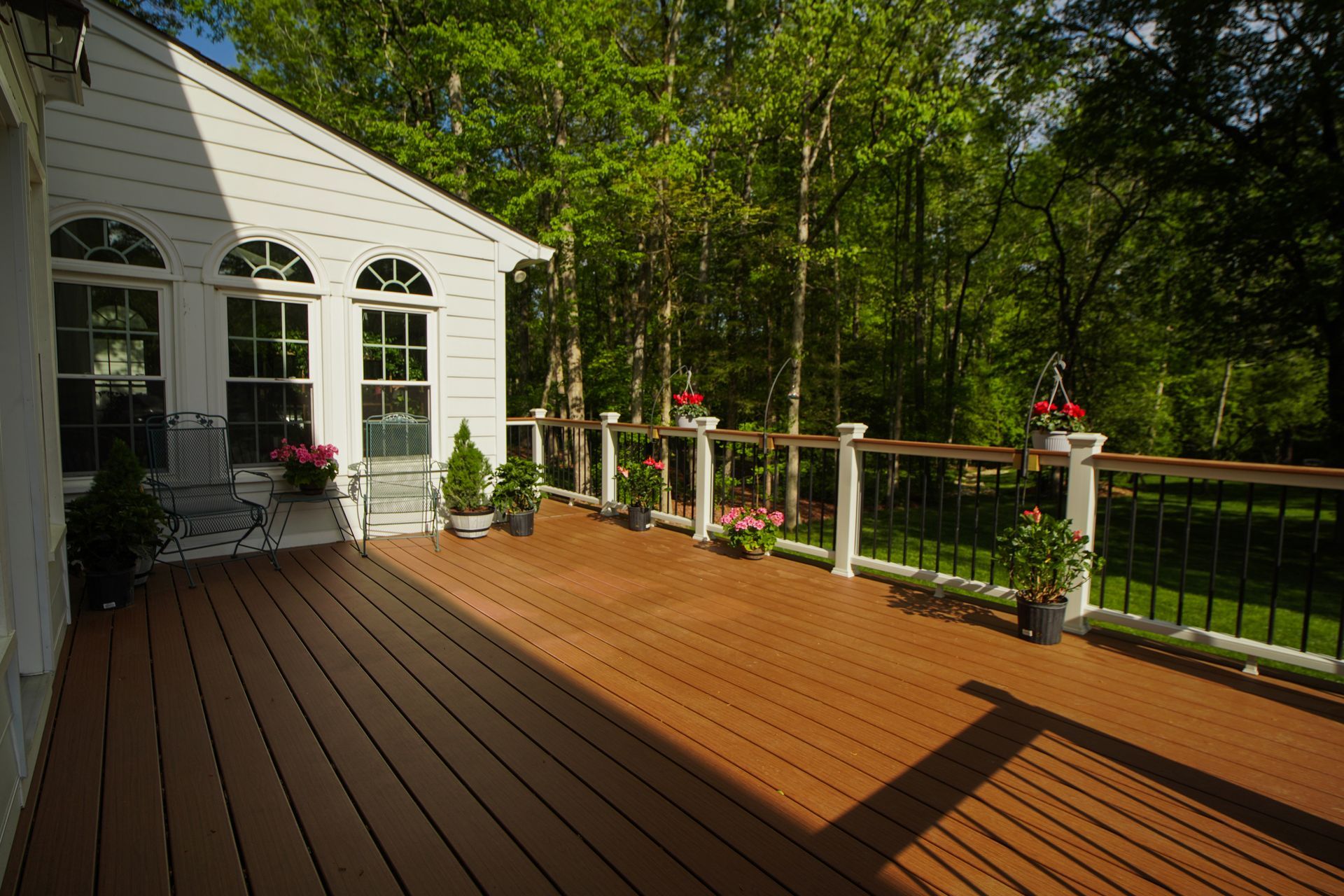 A modern backyard deck with outdoor seating, connected to a brightly lit home interior by large, open folding glass doors.