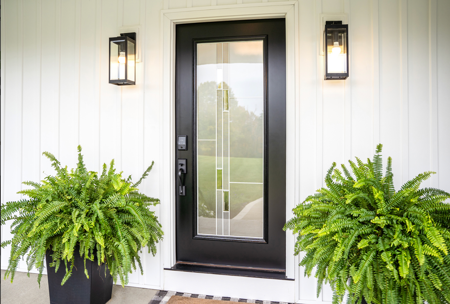 A wooden porch with white railings and columns, featuring hanging green plants and dark shutters on a sunny day.