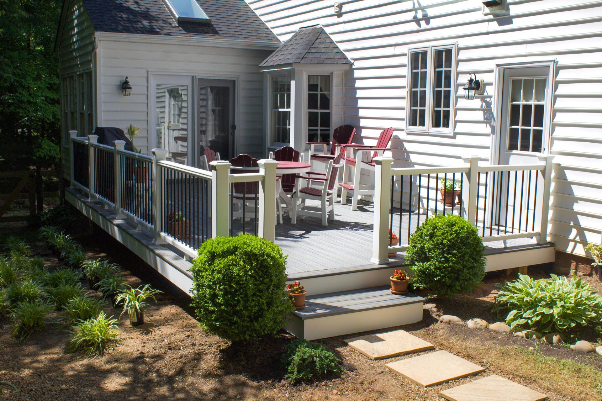 A bright, covered patio with tiled floors, featuring outdoor seating, a dining table, and large windows with garden views.