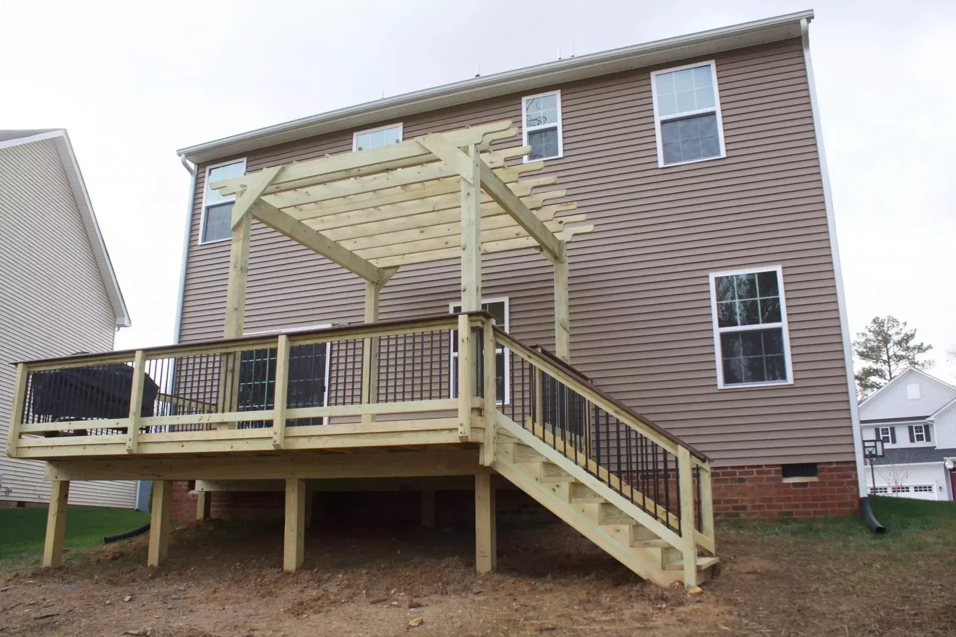 A newly constructed wooden deck featuring a pergola and stairs, attached to the back of a two-story beige vinyl-sided home.