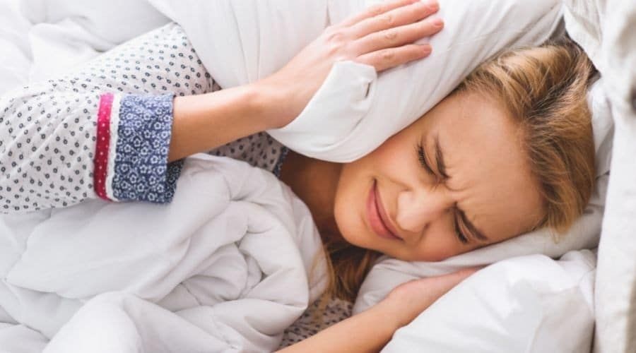 woman covering her ears with pillow