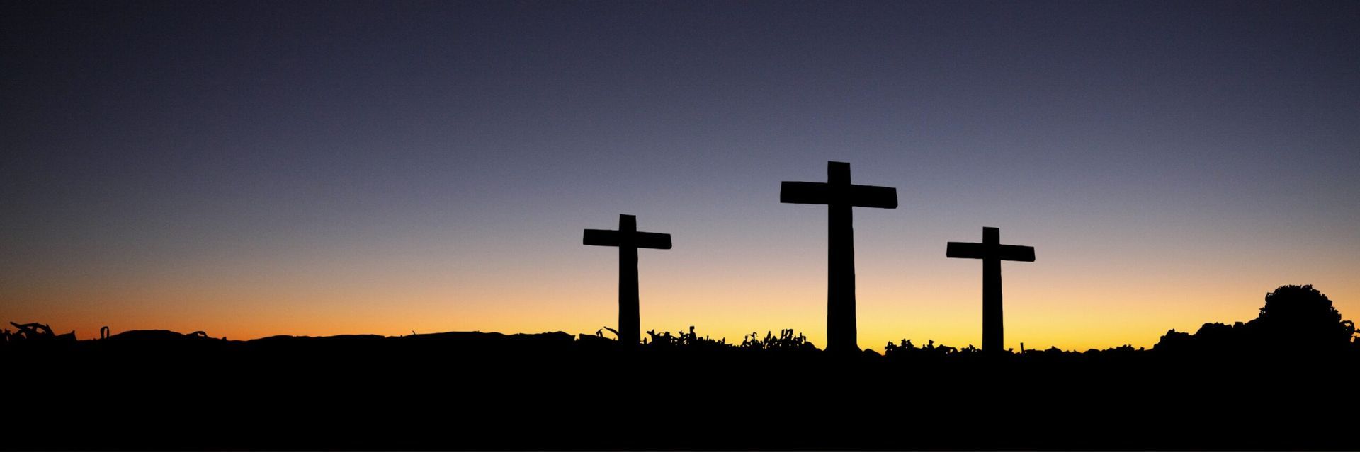 three crosses standing in silhouette against sunset sky