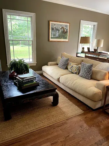 A light-colored sofa with patterned cushions sits in a living room next to a dark wood coffee table on a woven rug.