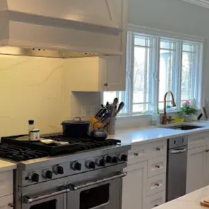 A modern white kitchen featuring a stainless steel stove, range hood, built-in microwave, and marble-style countertops.