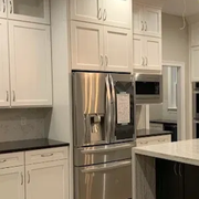 A modern kitchen featuring white upper cabinetry, stainless steel appliances, and a dark island with white countertops.