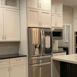 A modern kitchen featuring white upper cabinetry, stainless steel appliances, and a dark island with white countertops.