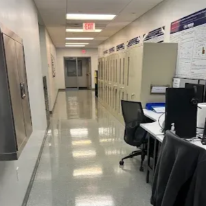 An office hallway with a polished floor, lockers on the right, and workstations with computers.