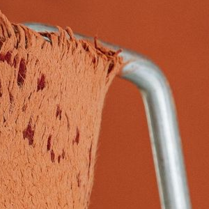 A paint roller covered in orange paint rests on top of a worn, white wooden stepladder against a matching orange wall.