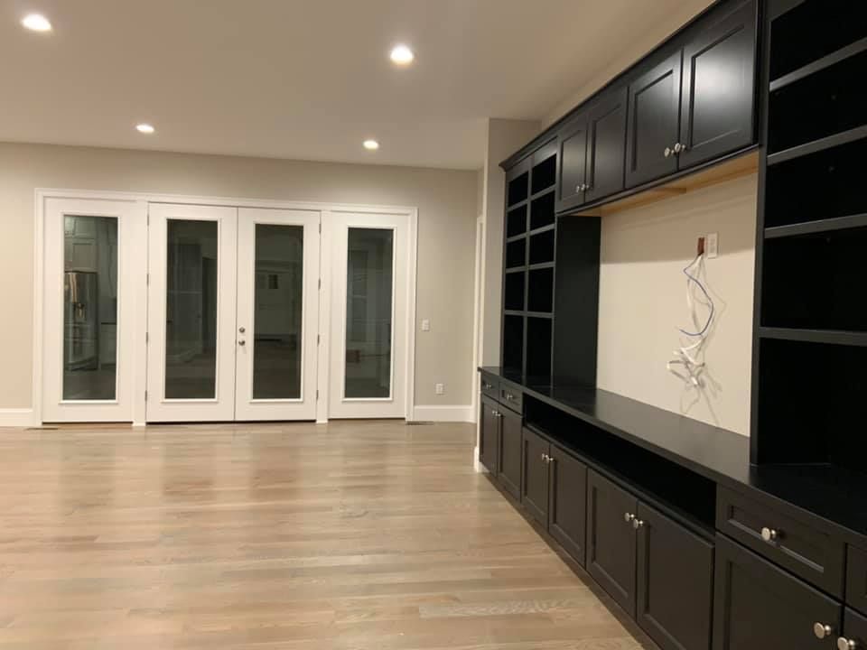 Modern living room featuring light hardwood floors, white-framed French doors, and a large black built-in wall unit.