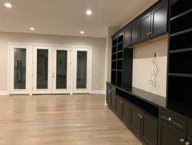 Modern living room featuring light hardwood floors, white-framed French doors, and a large black built-in wall unit.