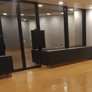 A spacious, modern room featuring polished hardwood floors, recessed lighting, and large glass windows.