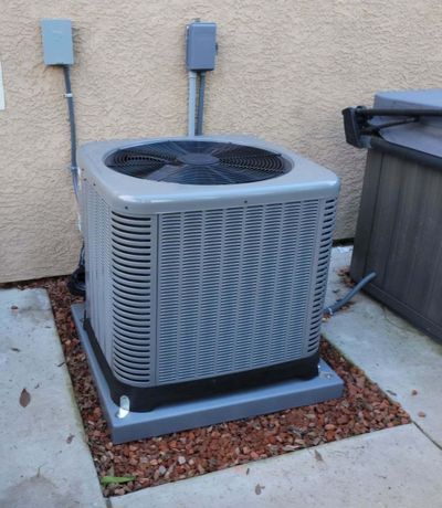 A large air conditioner is sitting on a sidewalk next to a hot tub