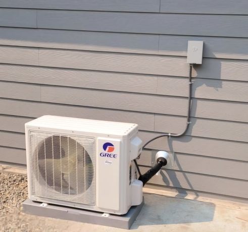 A gree air conditioner is mounted to the side of a house
