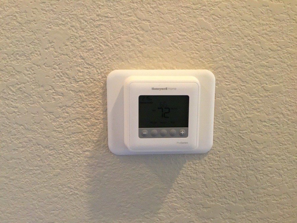 A white thermostat is mounted on a white wall.