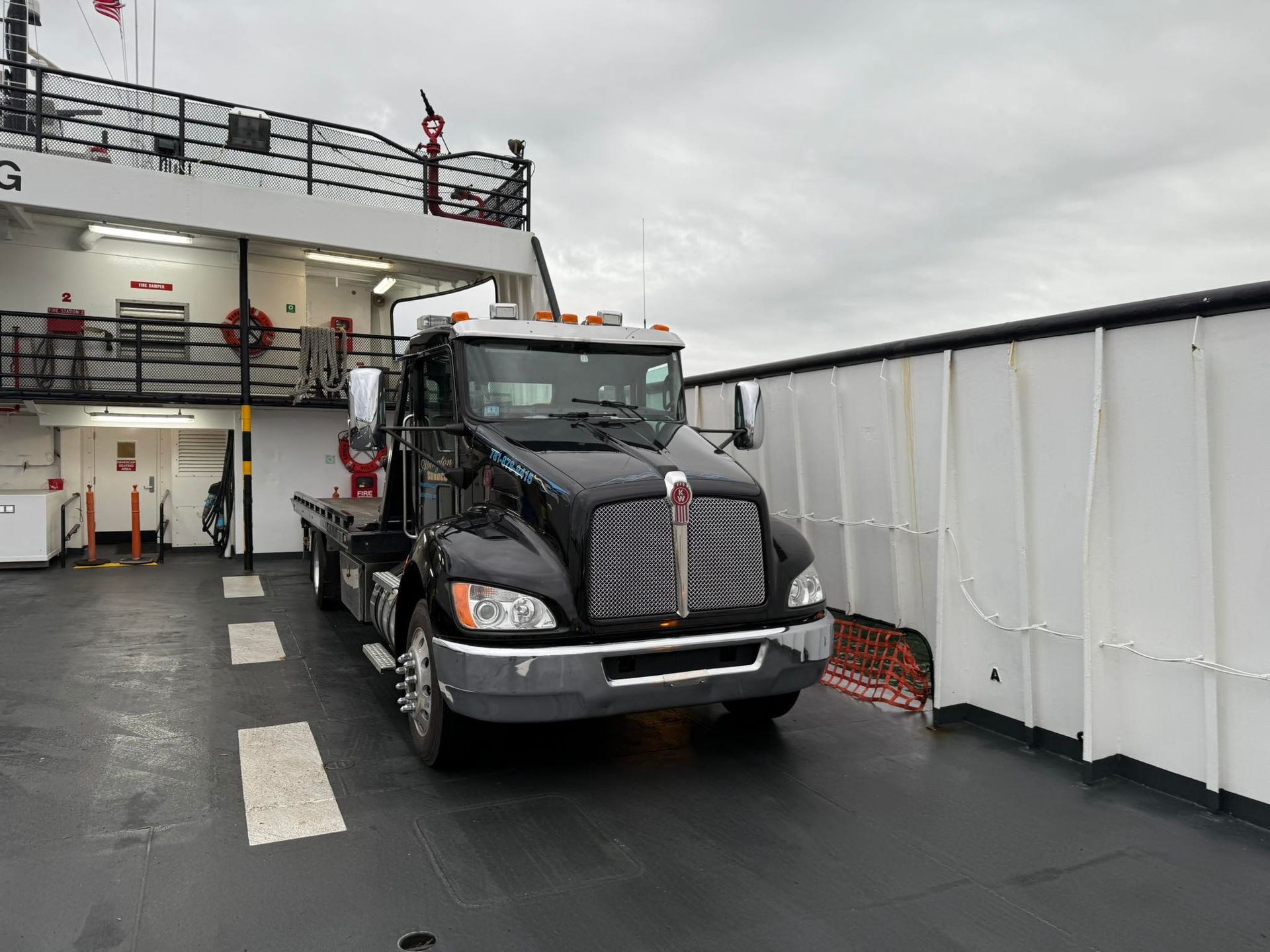 A black tow truck is parked on the deck of a boat.