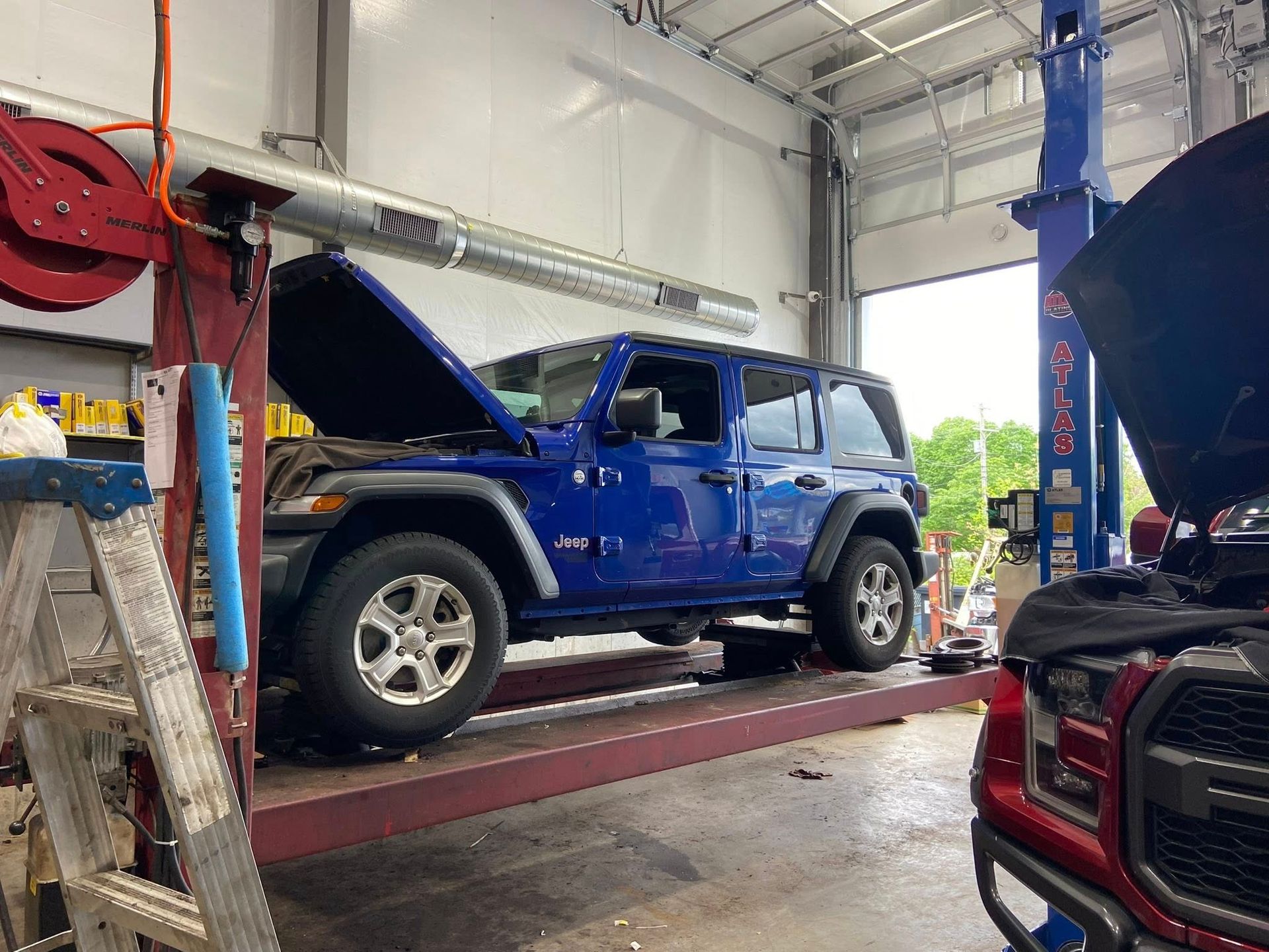 A blue jeep is sitting on a lift in a garage with its hood open.