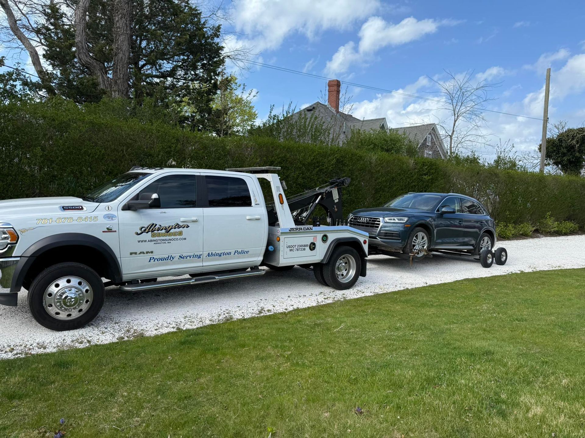 A white tow truck is towing a black car on a gravel road.