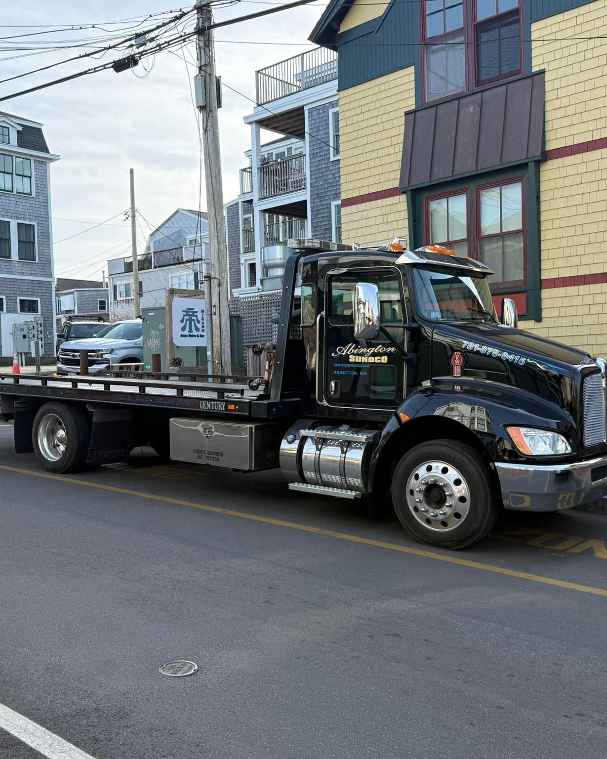 A black tow truck is parked on the side of the road in front of a building.