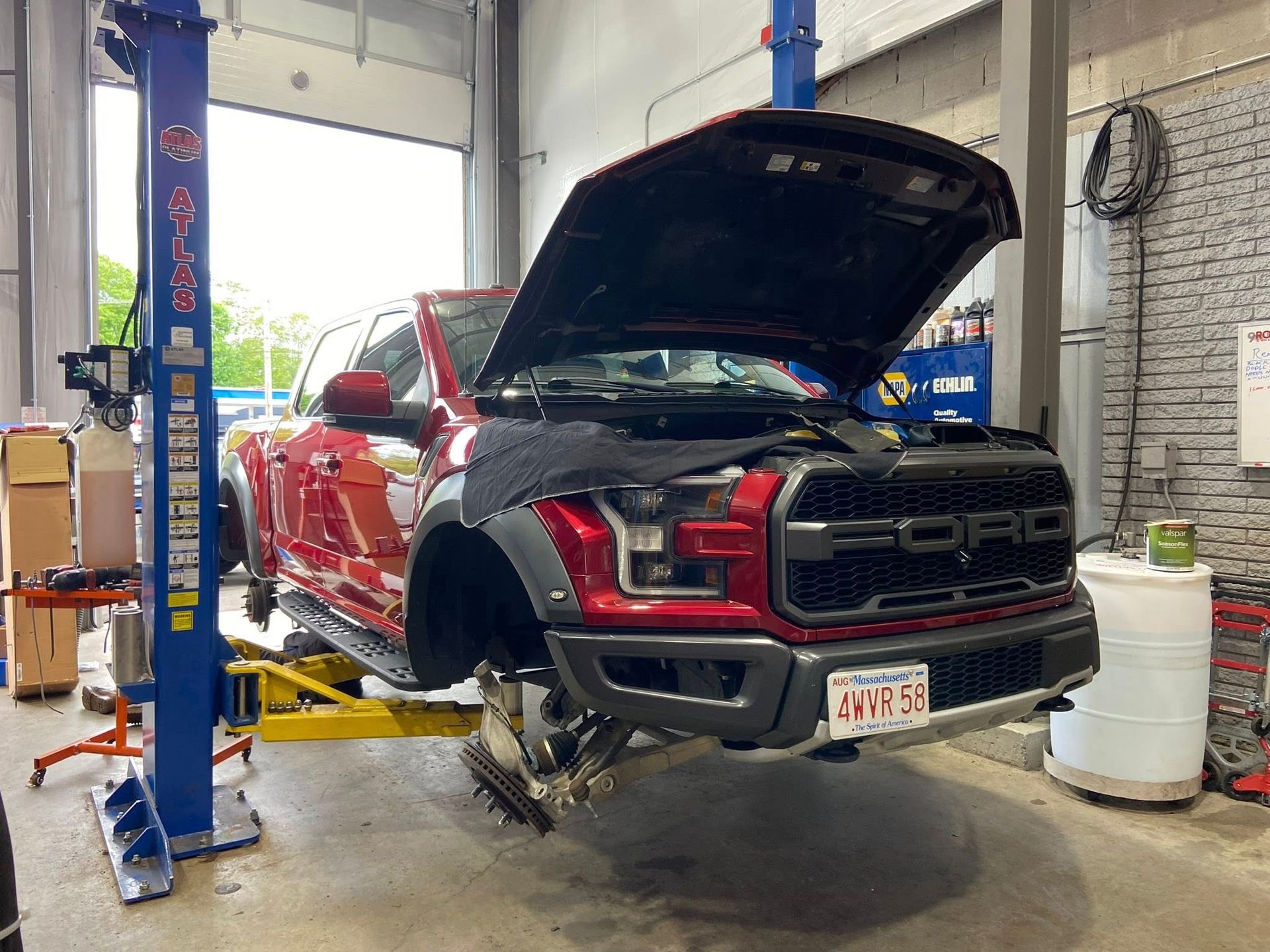 A red ford raptor is sitting on a lift in a garage.