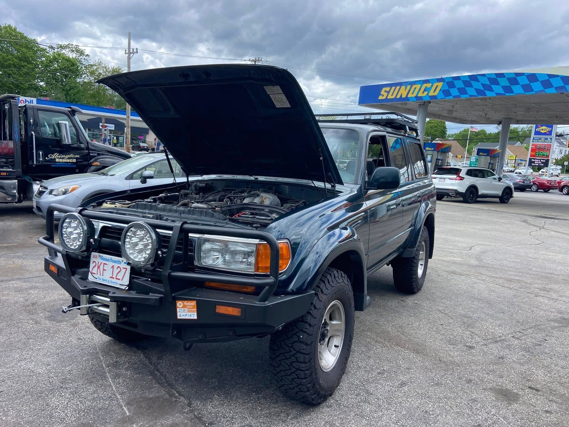 A black suv with the hood up is parked in front of a gas station.