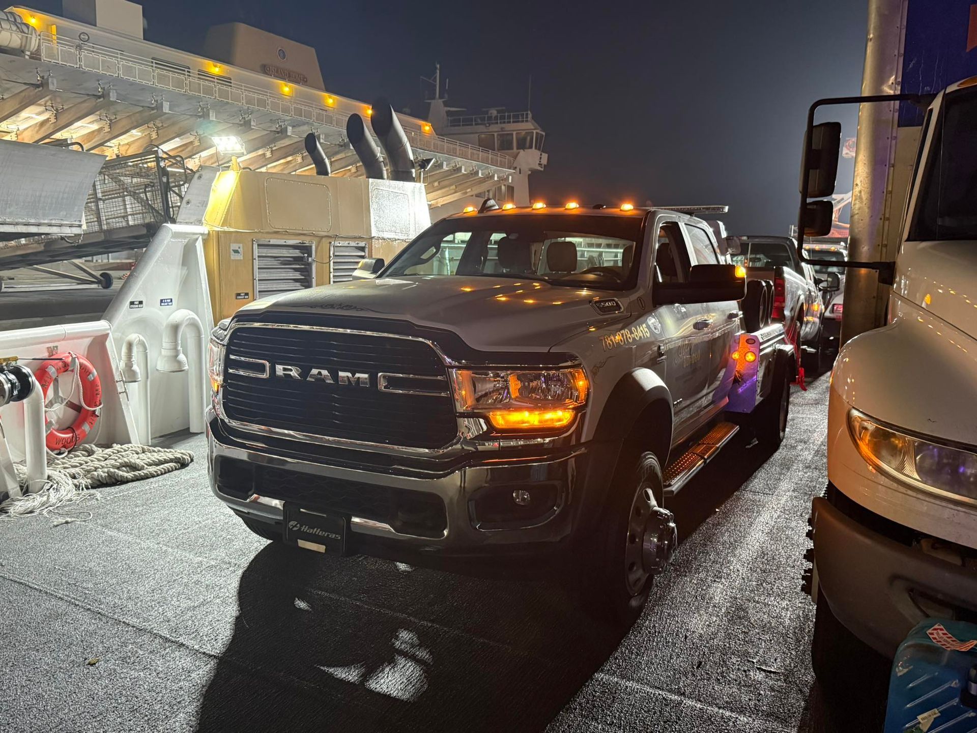 A large, silver Ram pickup truck on a ferry at night, surrounded by other vehicles and icy structures.