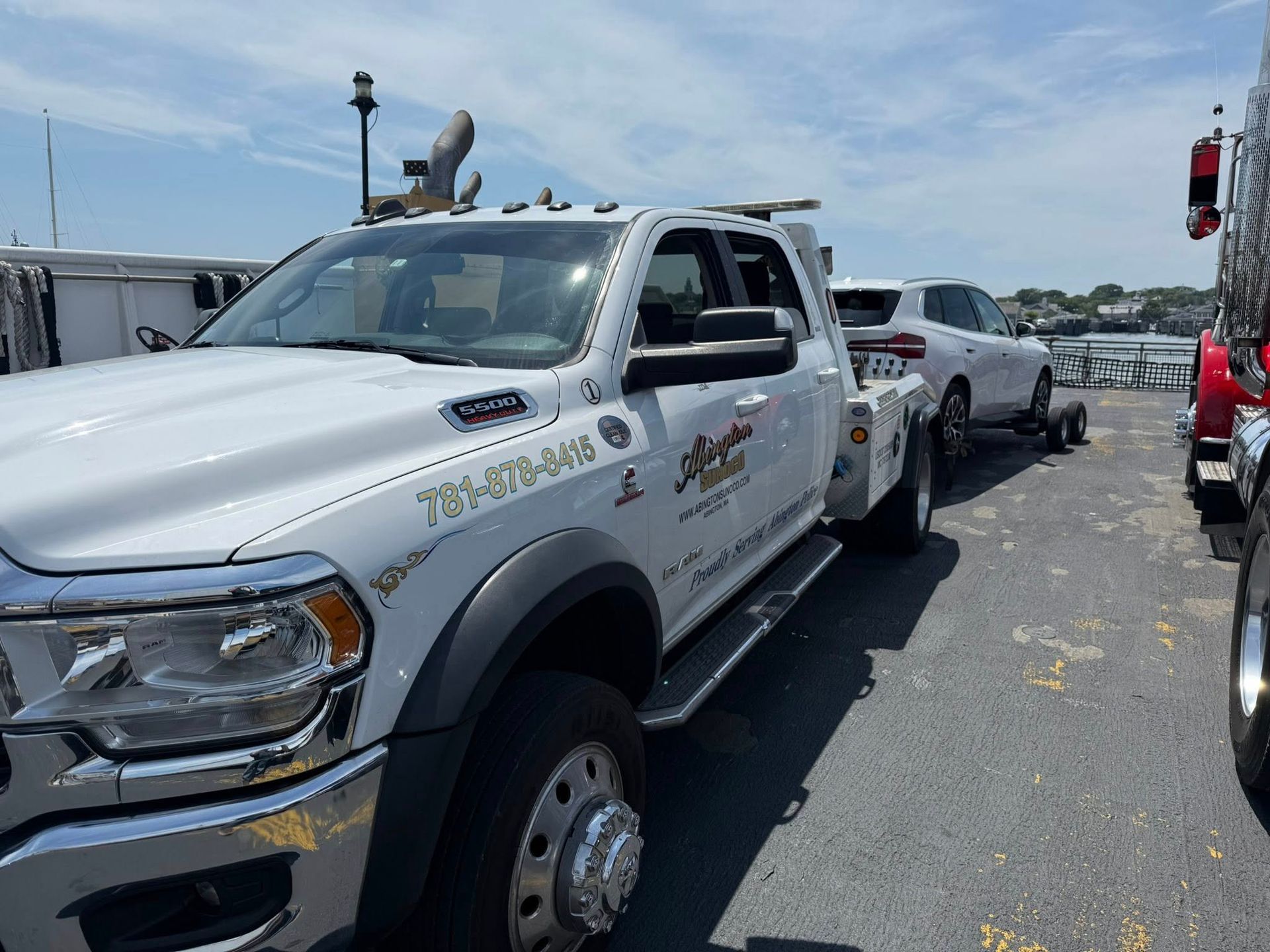 White tow truck towing a white SUV on a sunny day; outdoors near a body of water.