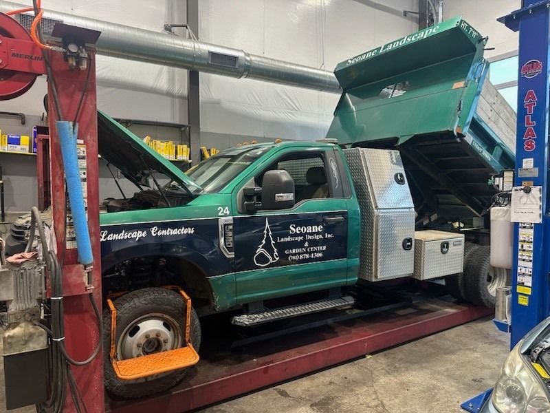 Green and blue dump truck in a mechanic shop with the hood open.
