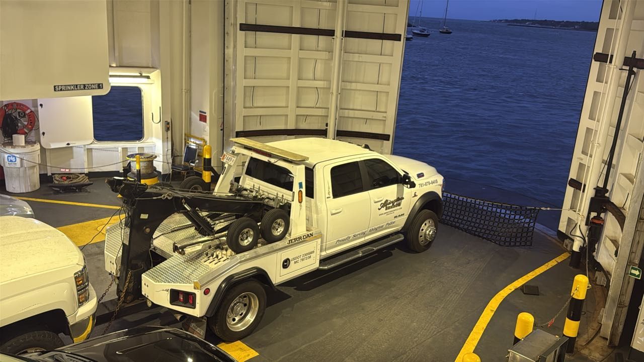 A white tow truck on a ferry, close to the open sea.