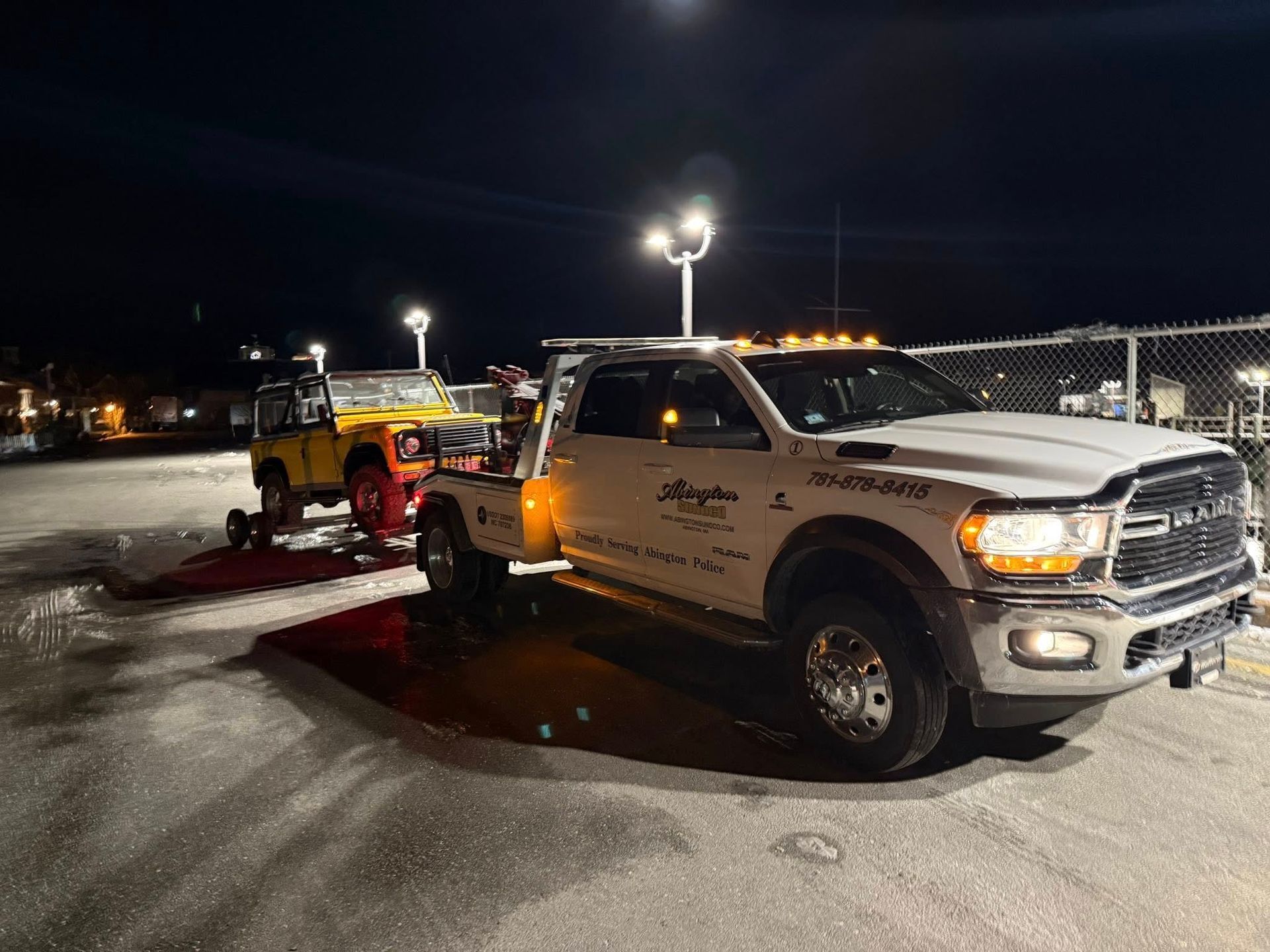 Tow truck loading a yellow vehicle onto its bed at night.