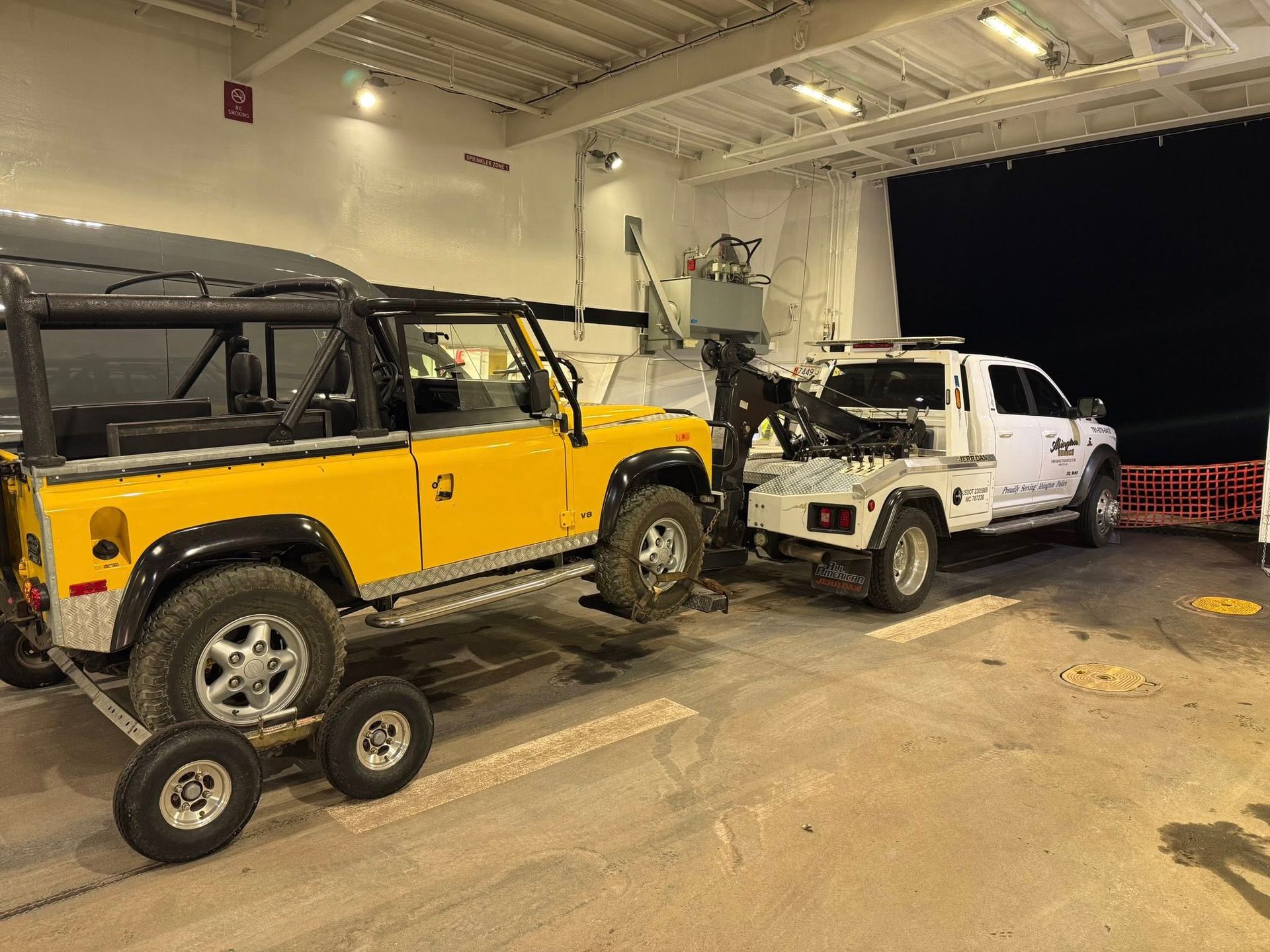 Yellow Land Rover being towed by a white tow truck on a ferry.