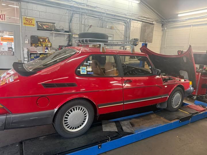 Red Saab 900 in a repair shop with hood open, parked on a blue lift.