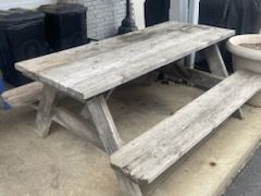 A wooden picnic table with two benches is sitting on a sidewalk.