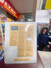 A woman is standing behind a counter with a newspaper on it.