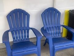 Two blue plastic lawn chairs are sitting next to each other on a sidewalk.