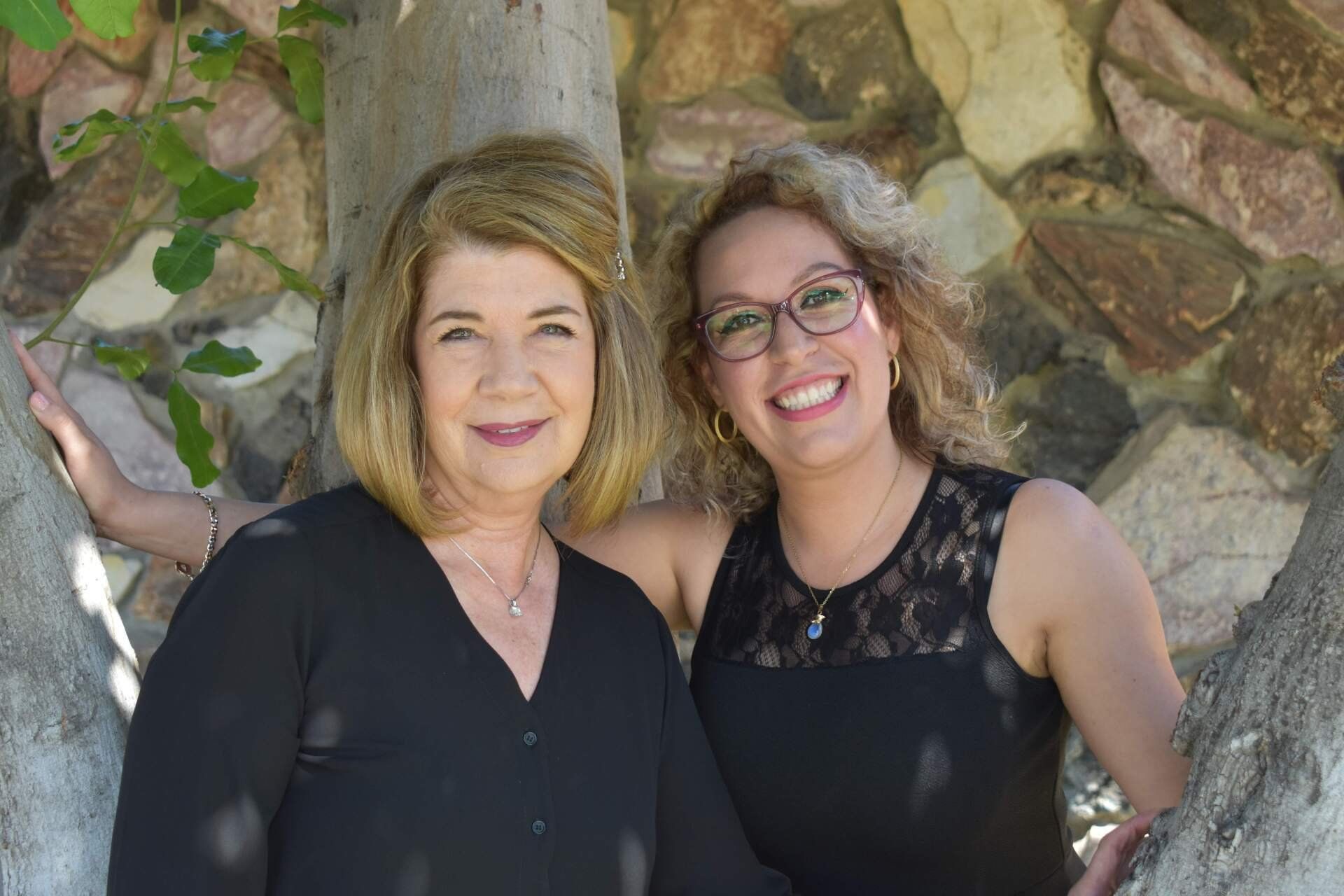 Two women are posing for a picture in front of a tree.