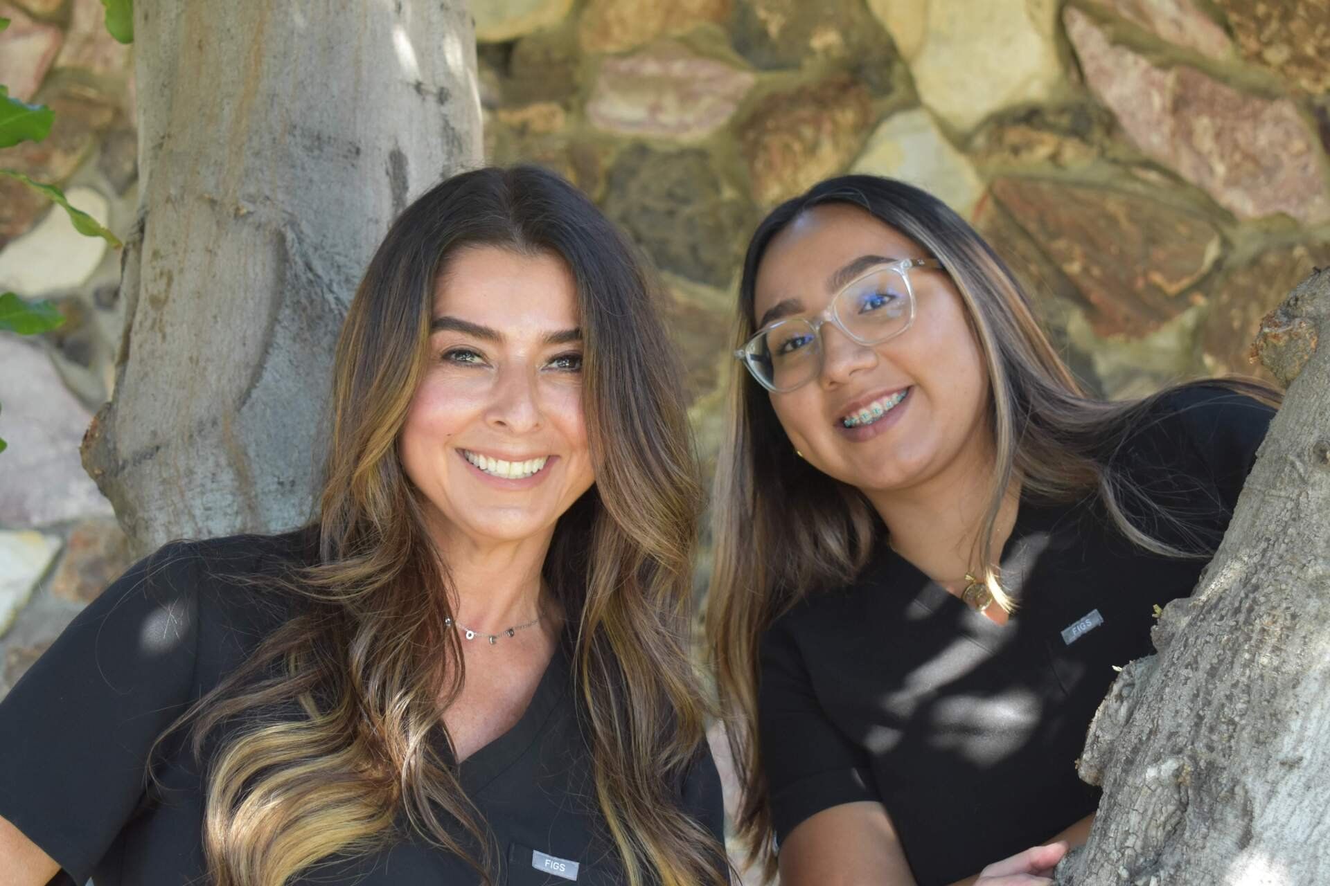 Two women are posing for a picture next to a tree.