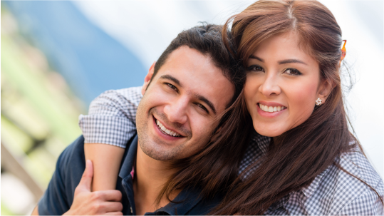 A man is carrying a woman on his back and they are smiling for the camera.