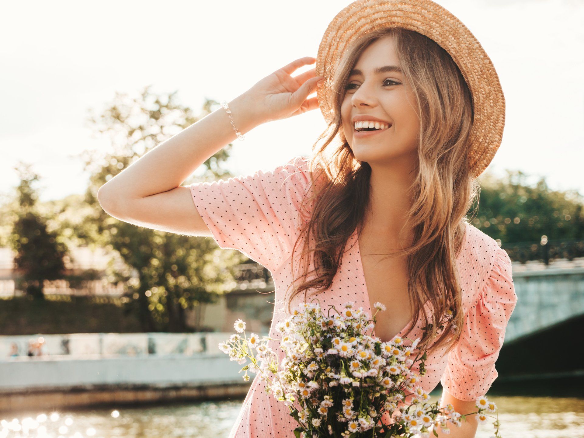 A woman in a pink dress and straw hat is holding a bouquet of flowers.