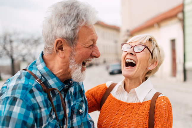 An elderly couple is laughing together while walking down the street.